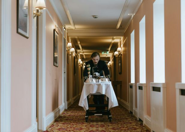 A hotel staff member pushes a room service trolley in a luxurious corridor.